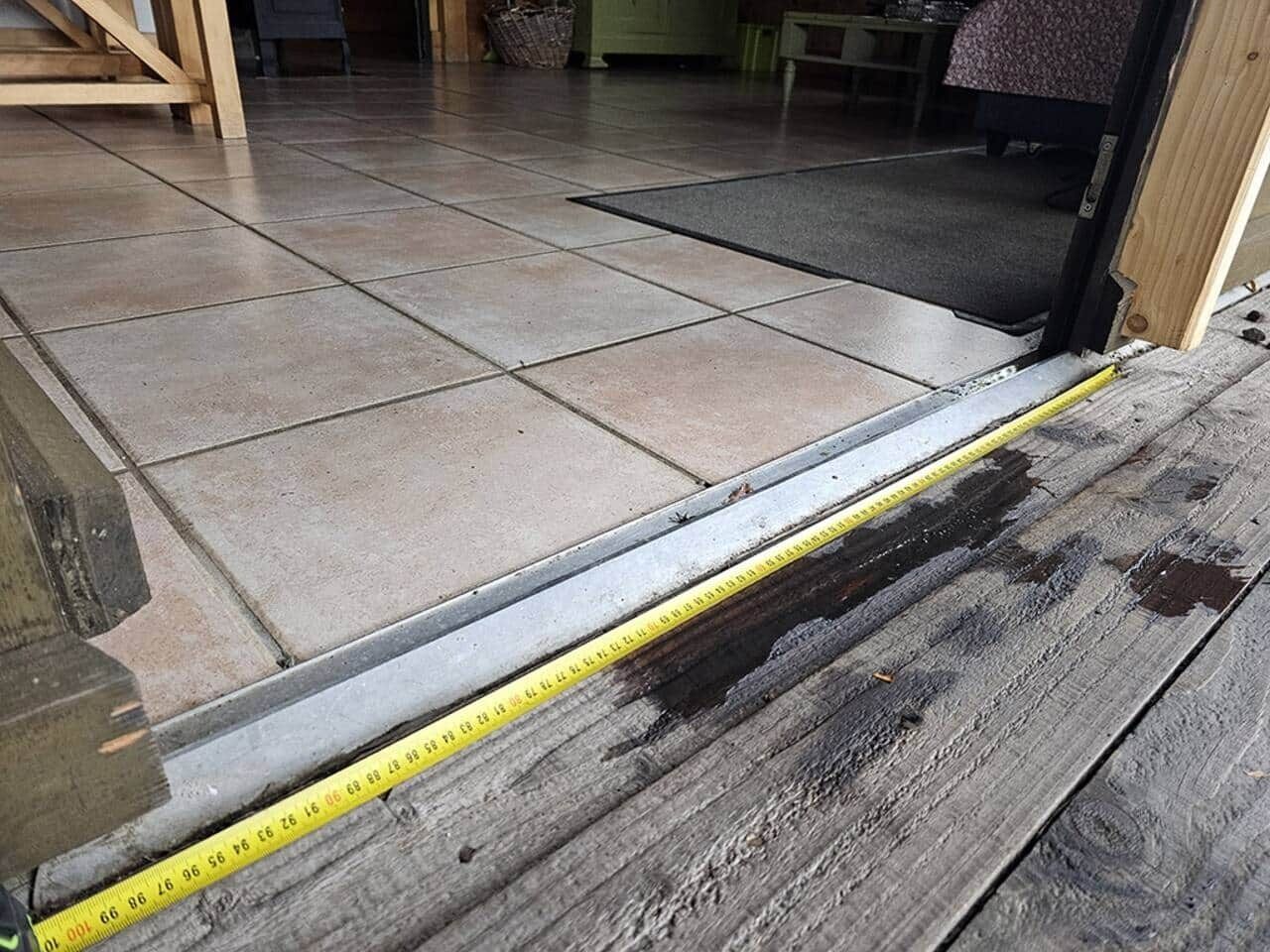 A measuring tape on a wooden floor next to a tiled area.