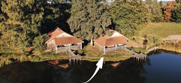 Two wooden cabins with red roofs, connected by a dock, situated by a calm lake surrounded by trees. - Le Fayard - Chalet with terrace (Mélisey)