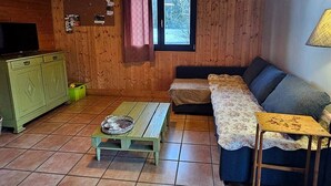 A cozy room with wooden walls, a green cabinet, a sofa, a small table, and a window with curtains. - Le Fayard - Chalet with terrace (Mélisey)