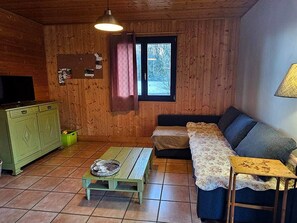 Ein gemütliches Zimmer mit Holzwänden, einem grünen Schrank, einer Couch, einem kleinen Tisch und einem Fenster mit Vorhängen.