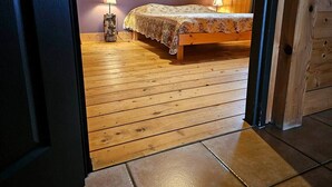 A bedroom with a wooden floor, a bed with a floral bedspread, a wall-mounted circular decoration, and a nightstand with a lamp. - Le Fayard - Chalet with terrace (Mélisey)