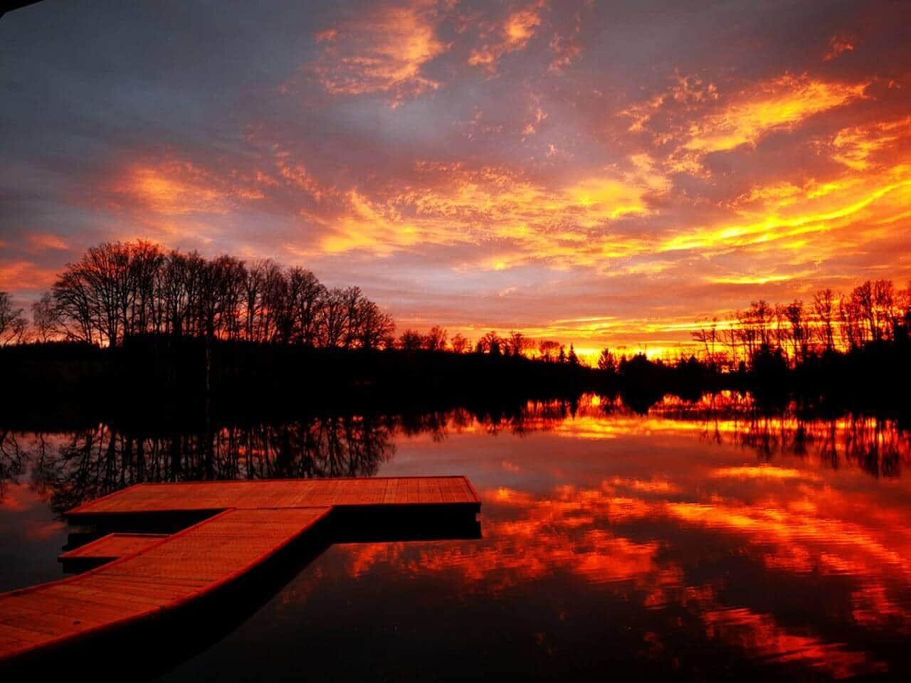 Un coucher de soleil sur une étendue d’eau calme, avec une jetée en bois.