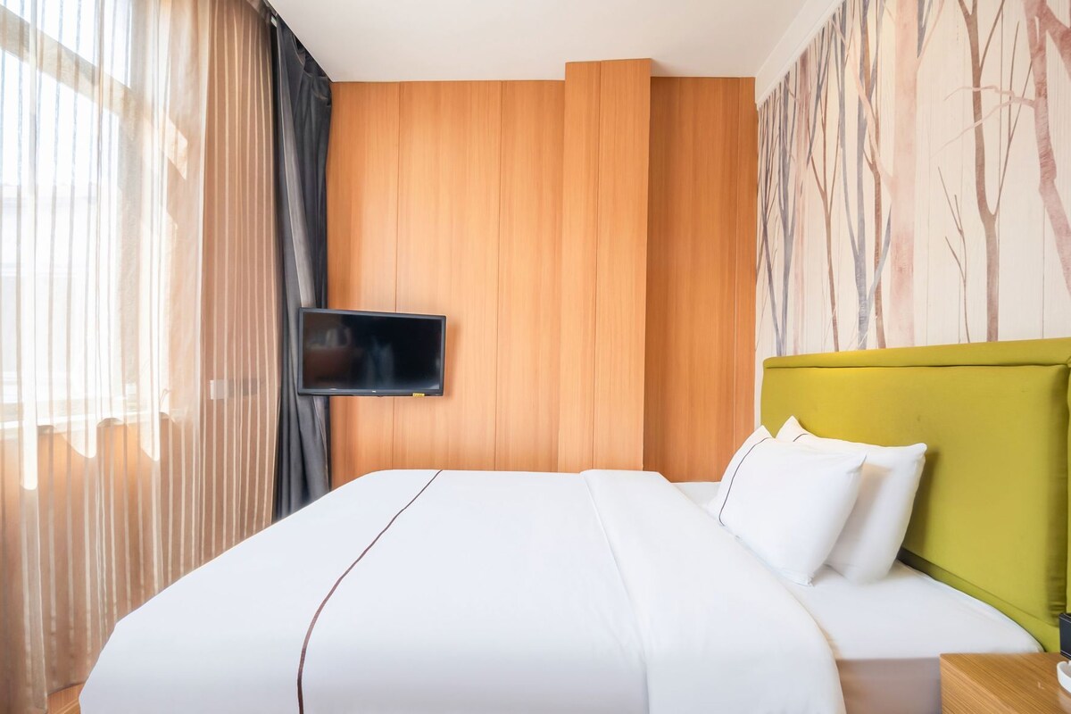 A hotel room with a large bed, a flat-screen TV mounted on the wall, and a green headboard.