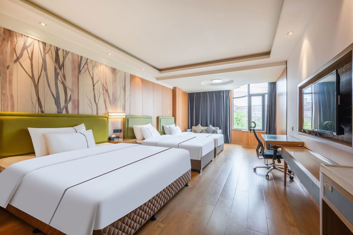 A hotel room with two beds, a desk, a TV, and a large window.
