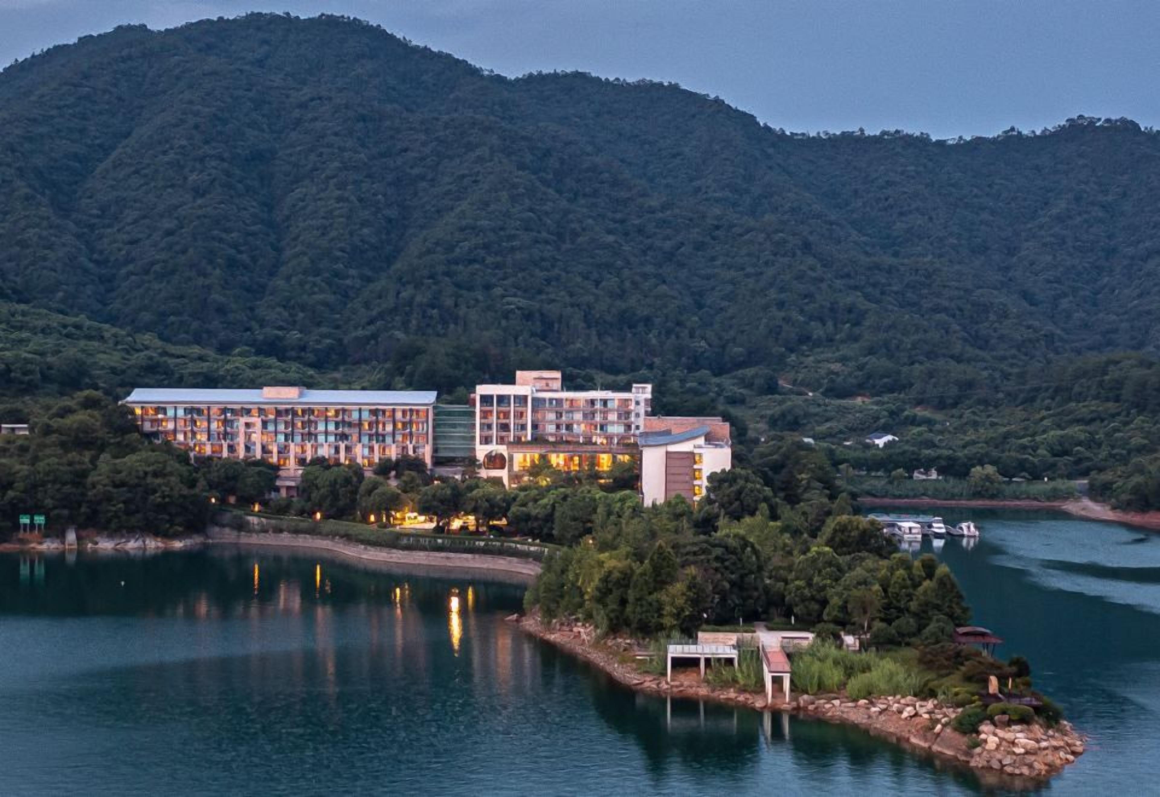 A hotel with multiple buildings by a lake, surrounded by forested hills.