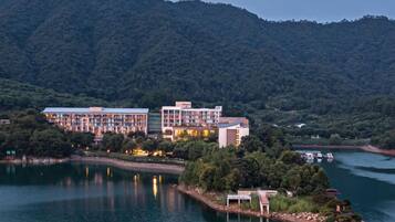 A hotel with multiple buildings by a lake, surrounded by forested hills.