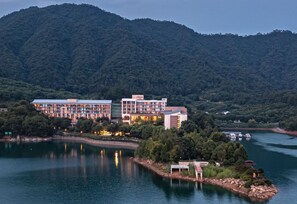 Un hotel con varias edificaciones junto a un lago, rodeado de colinas boscosas.