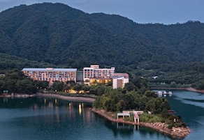 A hotel with multiple buildings by a lake, surrounded by forested hills.