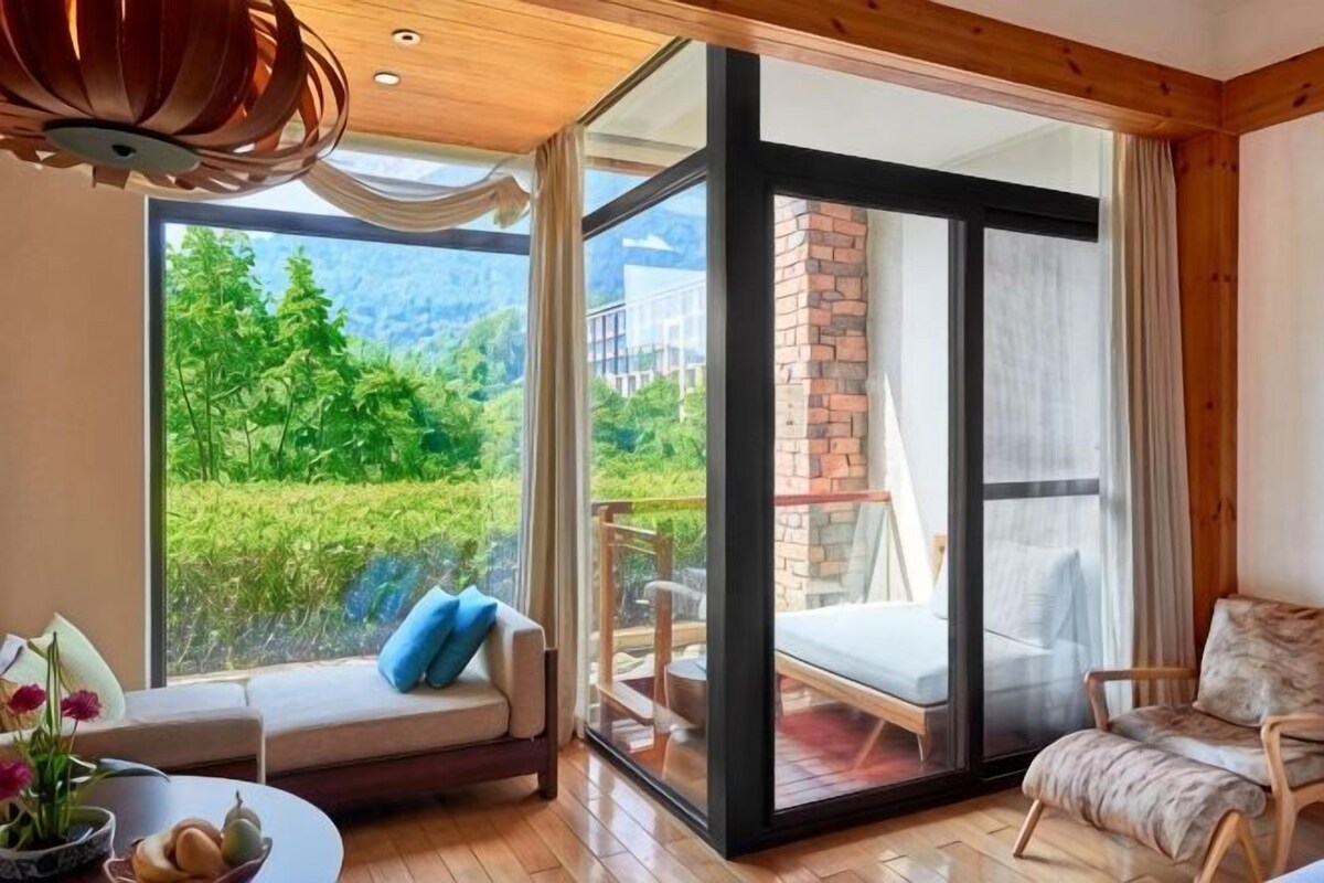 Ein Zimmer mit einer Schiebetür zu einem Balkon, einem Sofa, einem Sessel und einem Tisch mit Blumen.