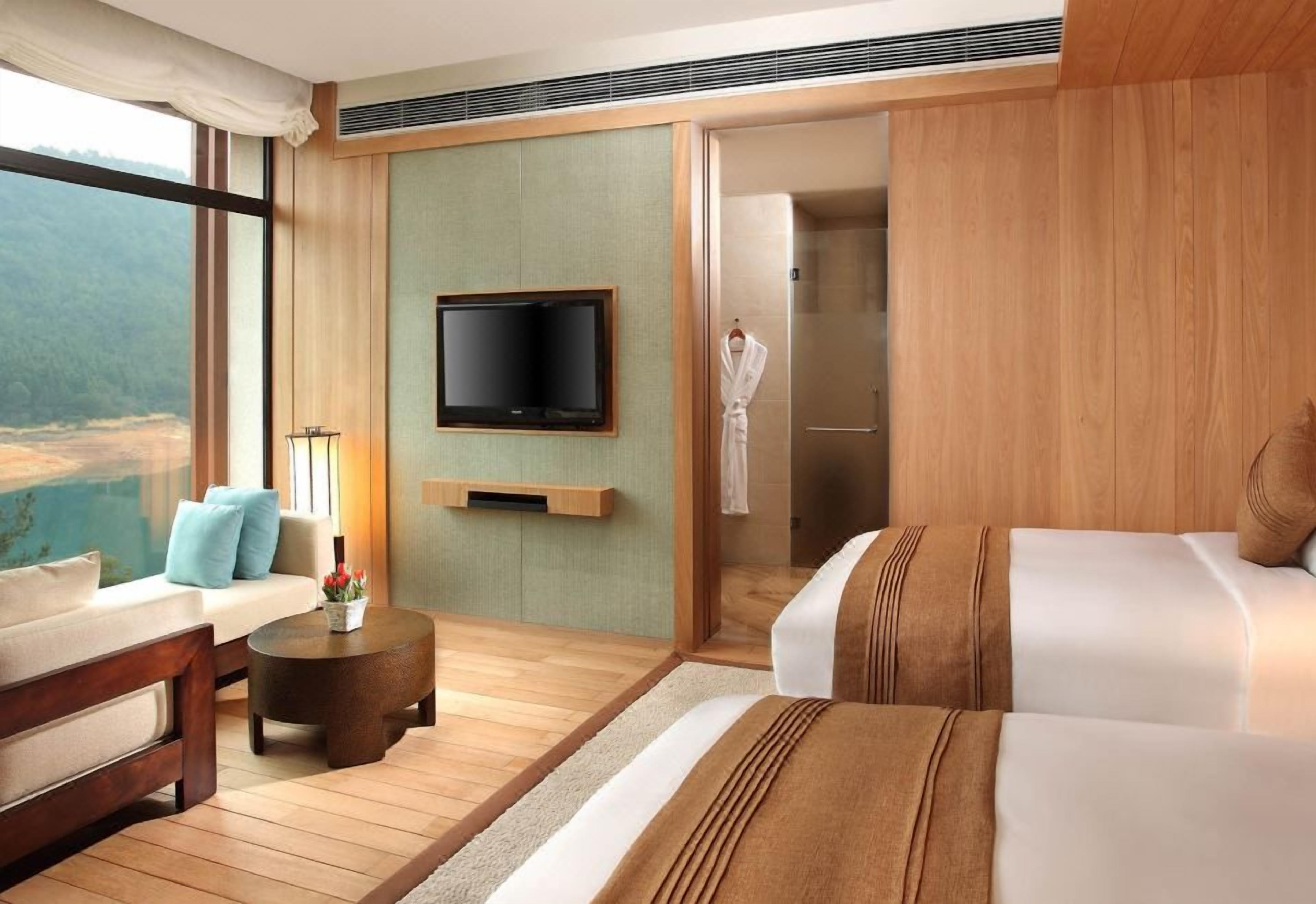 Habitación de hotel con un ventanal grande, televisión de pantalla plana, sofá, cama, mesita redonda pequeña y ducha a pie.