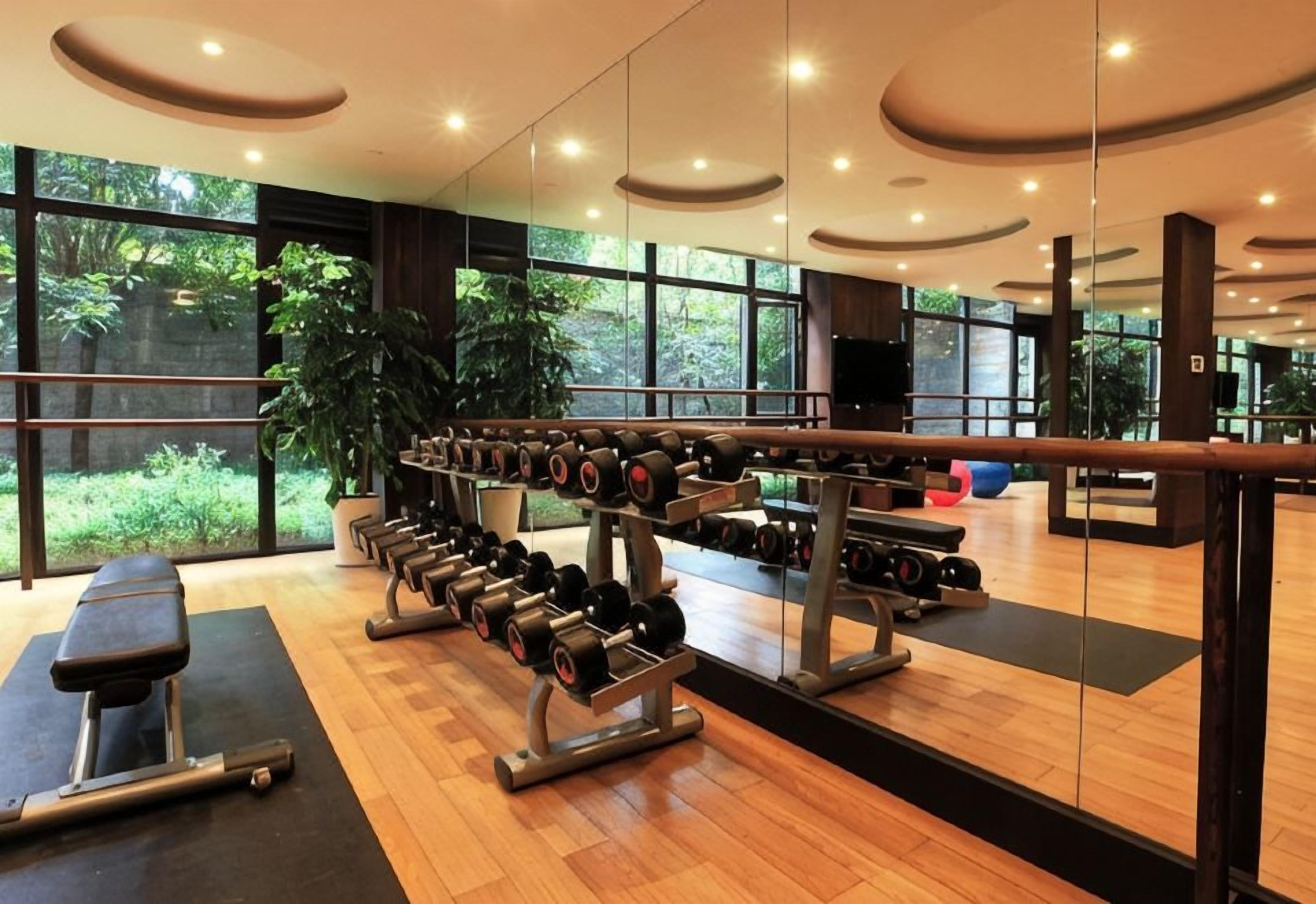 Un gimnasio con equipo de ejercicio, una banca y ventanas amplias.
