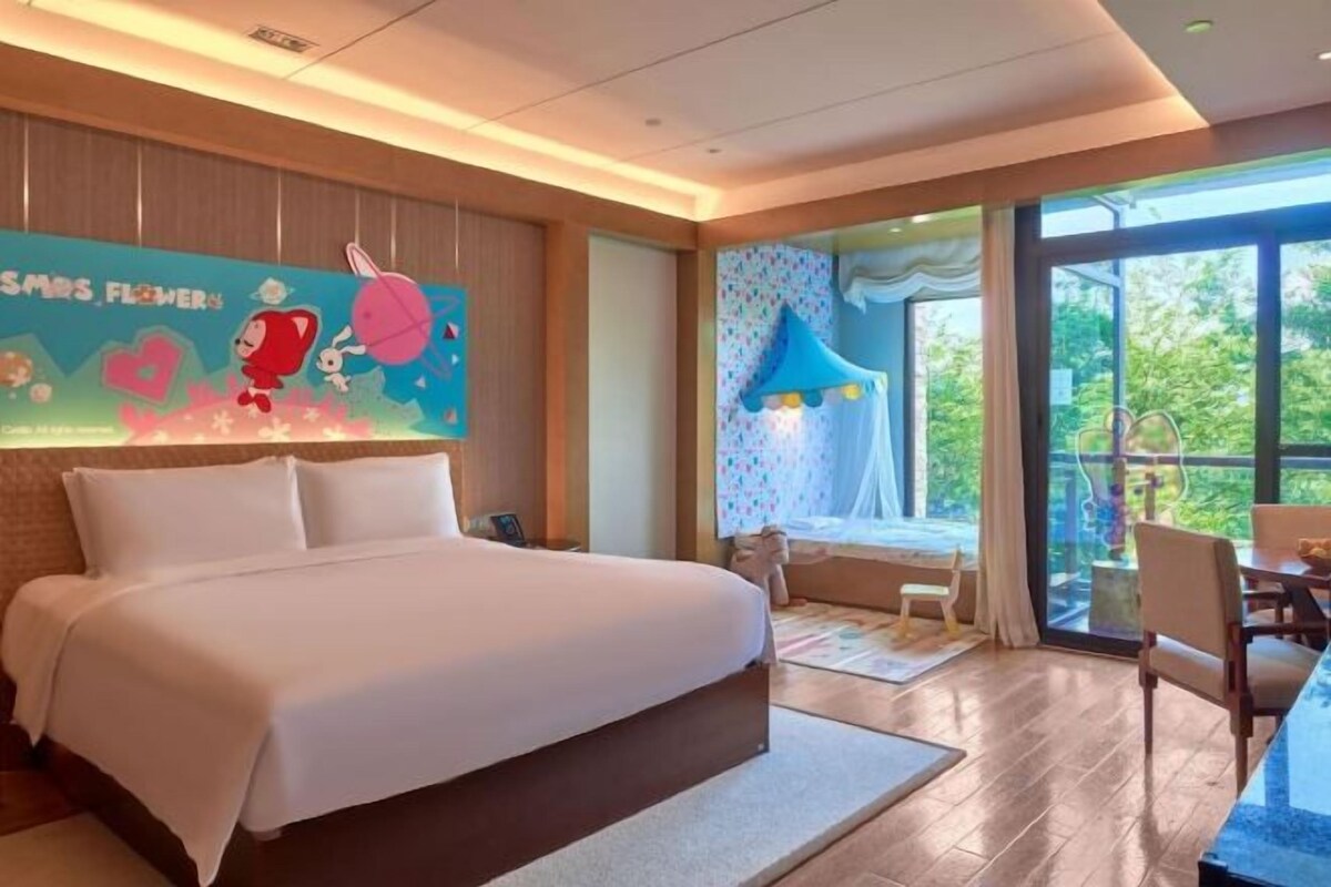 Habitación de hotel moderna con una cama grande, zona de comedor y vistas al exterior.