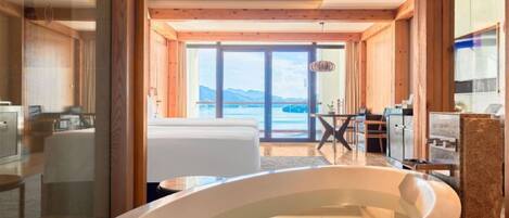 A modern bathroom with a large bathtub, wooden beams, and a view of the sea.
