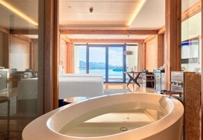 A modern bathroom with a large bathtub, wooden beams, and a view of the sea.