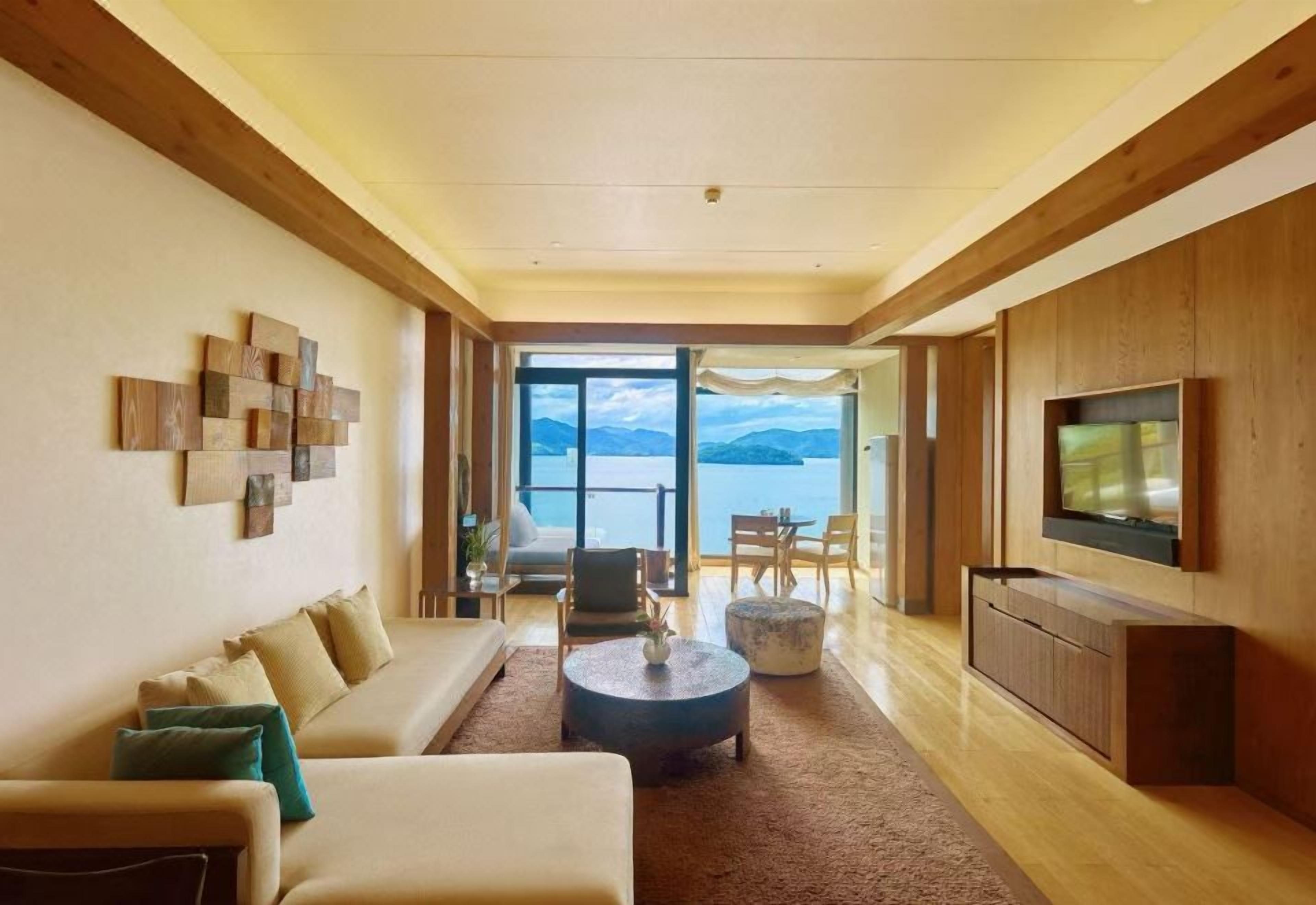 Una sala moderna con sofá, mesa de centro y televisor, que da a un balcón con vistas al mar.