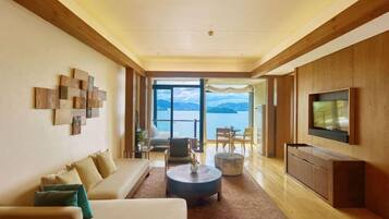 Una sala moderna con sofá, mesa de centro y televisor, que da a un balcón con vistas al mar.