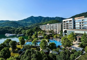 Een hotel met een zwembad, omringd door weelderige begroeiing en bergen.