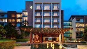 Un hôtel moderne doté d’une grande façade en verre, d’un espace extérieur couvert agrémenté d’une sculpture et d’une piscine.