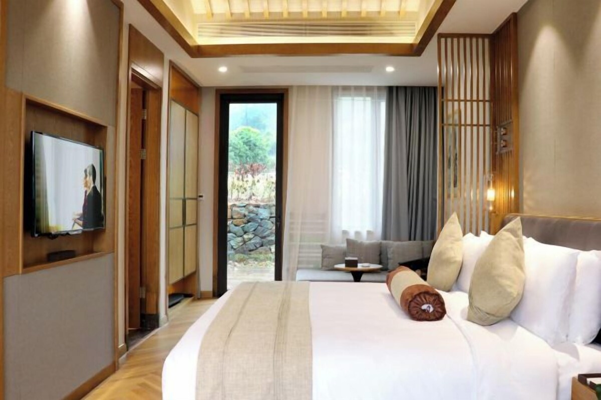 Habitación de hotel con una cama grande, televisor, sofá y vistas al exterior.