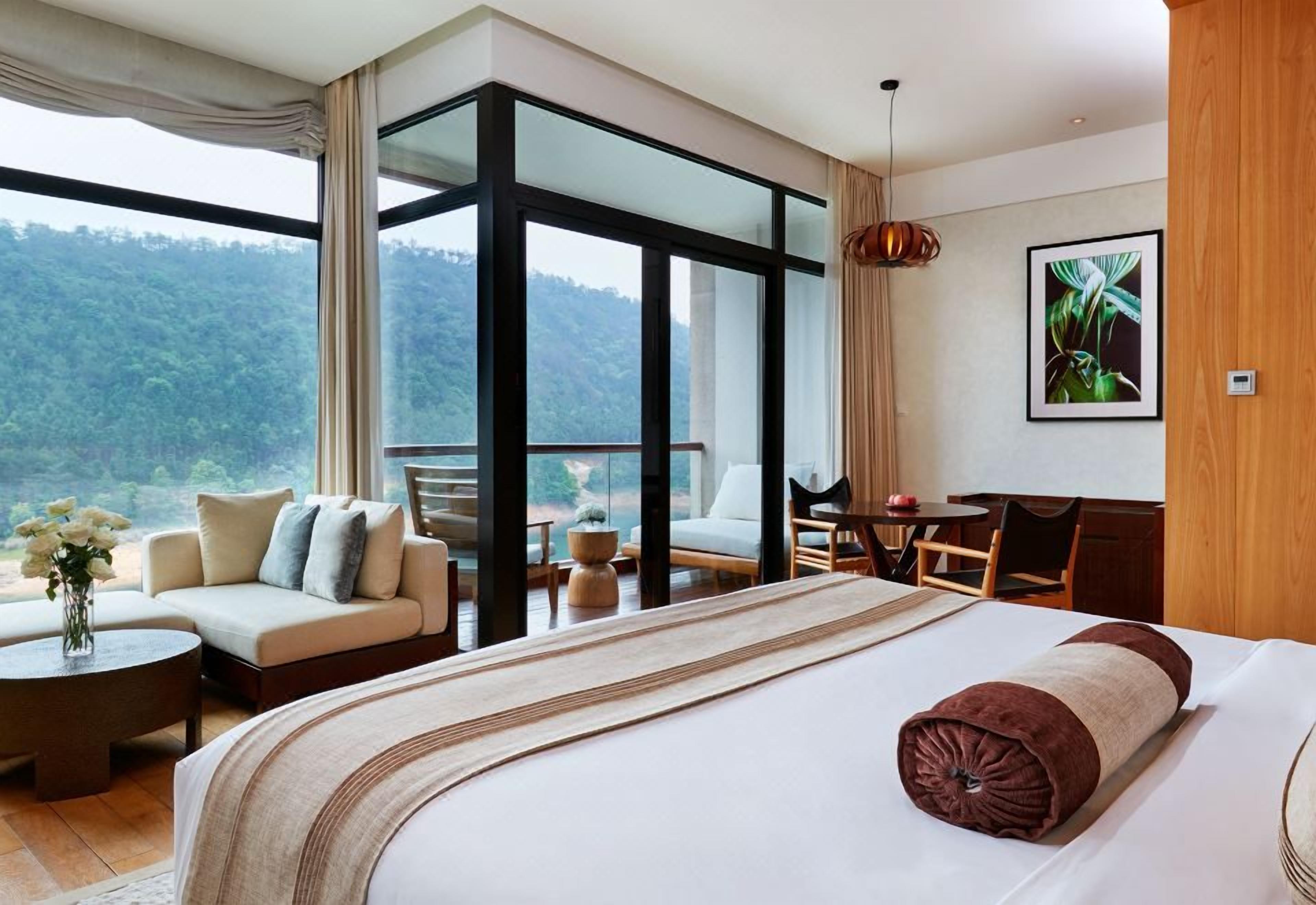 Ein Hotelzimmer mit einem großen Bett, einer Sitzecke, einem Schreibtisch und Blick ins Freie.