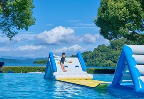 A child on a water slide in a pool with a clear sky and mountains in the background.
