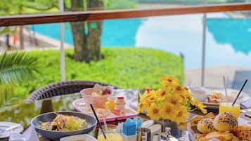 A breakfast table with various dishes, a vase of yellow flowers, and a view of a body of water.