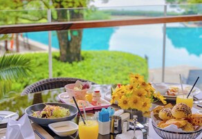 A breakfast table with various dishes, a vase of yellow flowers, and a view of a body of water.
