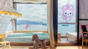 A room with a bed, a rocking horse, a chair, and a view of the sea through a glass door.