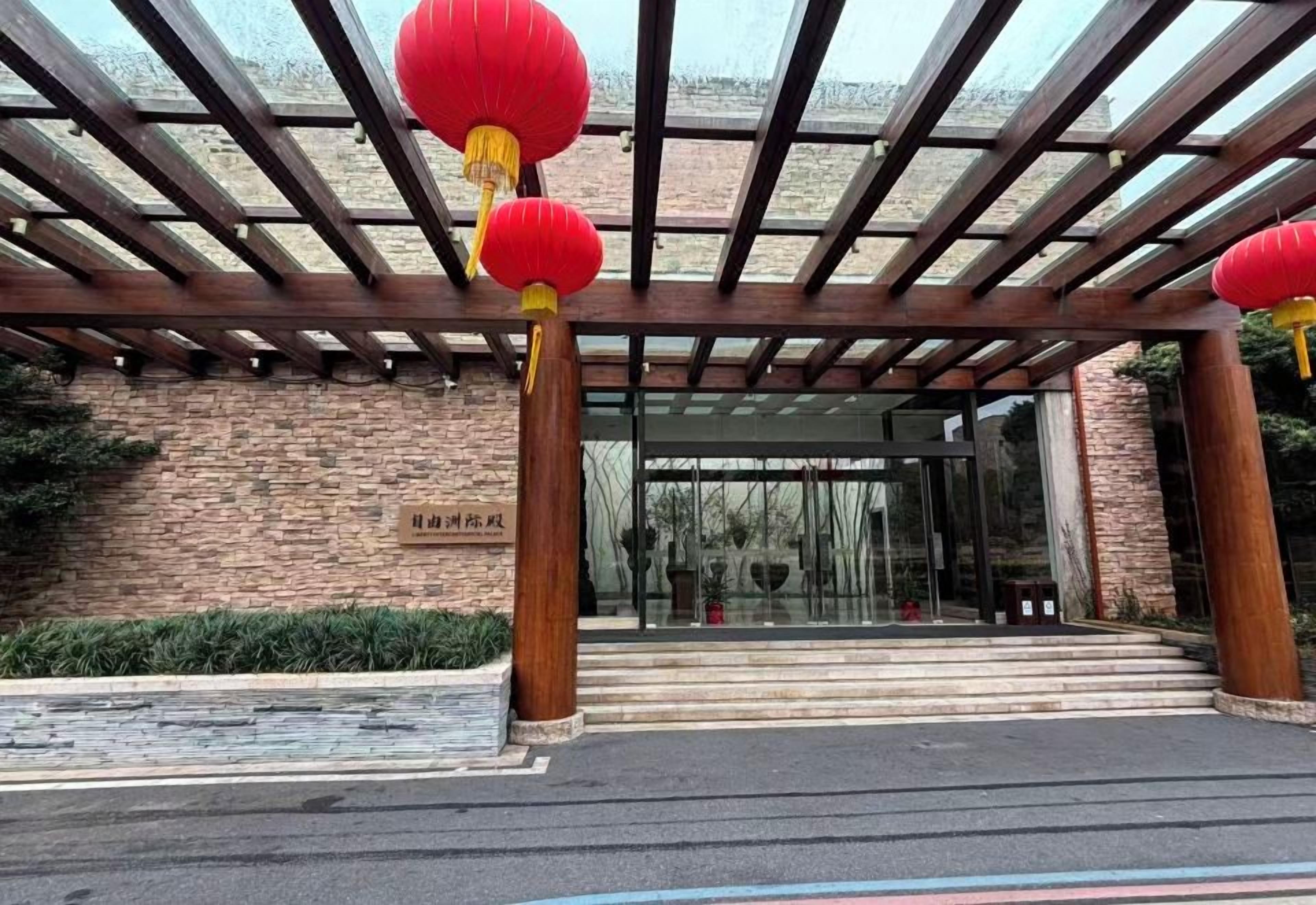 Entrada de edificio con una pérgola de madera, faroles rojos y una pared de ladrillo con un letrero.