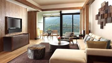 Una sala de estar moderna con un televisor de pantalla plana, un sofá, una mesa de centro y vistas a montañas a través de amplios ventanales.