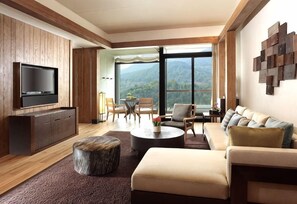Sala de estar moderna com televisão de tela plana, sofá, mesa de centro e vista para montanhas através de grandes janelas.