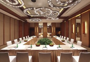 Un salón de conferencias con una larga mesa, sillas y una planta en el centro.