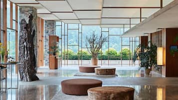A spacious lobby with a large stone sculpture, round seating, and large windows offering a view of greenery.