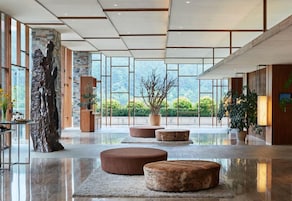 A spacious lobby with a large stone sculpture, round seating, and large windows offering a view of greenery.