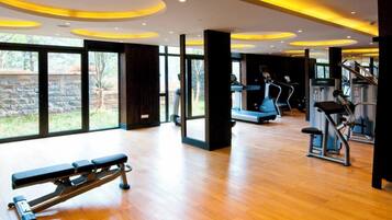 Un gimnasio con máquinas de cardio, una banca y ventanas amplias.