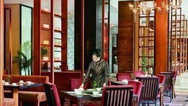 Un restaurant avec des meubles en bois, des chaises rouges et une personne assise à une table.