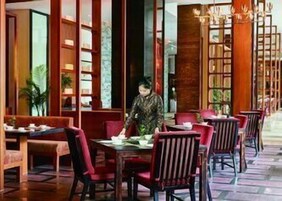 Un restaurante con mobiliario de madera, sillas rojas y una persona sentada en una mesa.