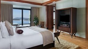 Une chambre d’hôtel avec un grand lit, une télévision, une vue sur la mer et une fenêtre.