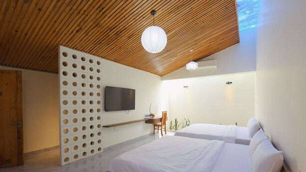 A modern hotel room with a wooden ceiling, a TV mounted on the wall, a desk with a chair, and two beds. - SON HAI HOMESTAY (Hue)
