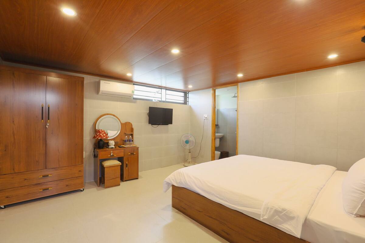 Un dormitorio con techo de madera, una cama, un tocador con espejo, una mesita y un televisor montado en la pared.