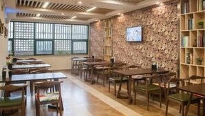 A restaurant with wooden tables and chairs, a stone wall with a television, and large windows. - Greentree Inn (Suzhou)