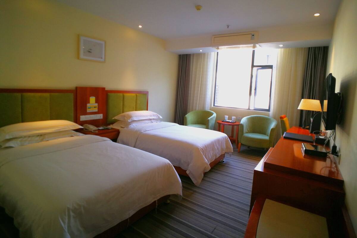 A hotel room with two beds, a desk, a chair, a television, and a window with curtains.