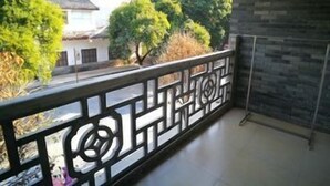 Un balcon orné d’une balustrade à motifs, une vue sur des arbres et un immeuble, et un mur en pierre.