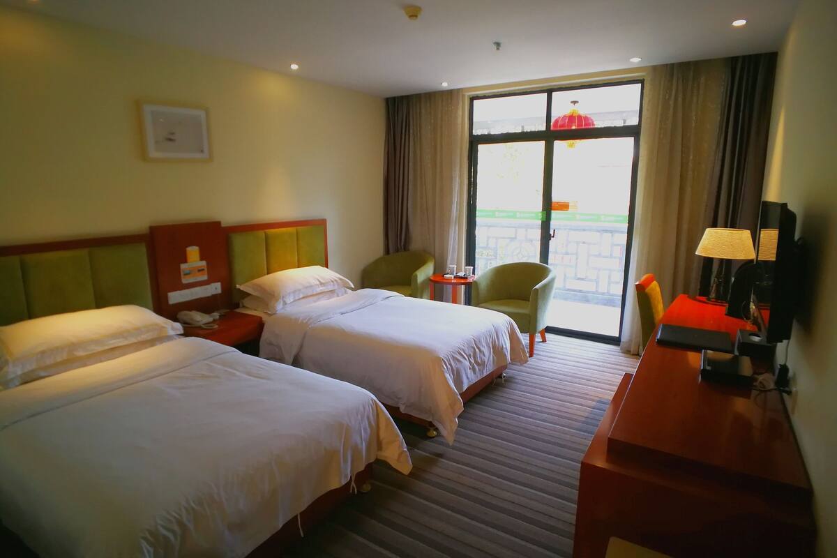 A hotel room with two beds, a desk, a chair, a lamp, and a window with a view.