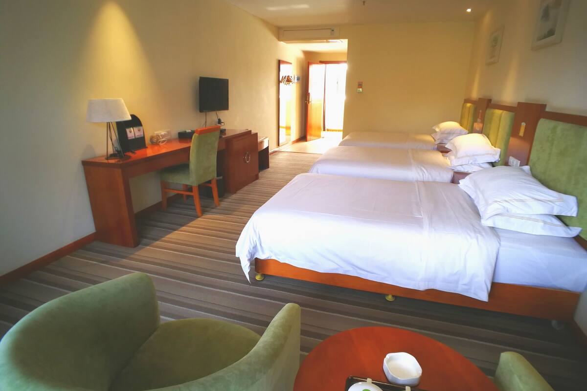 A hotel room with two beds, a desk, a chair, and a television.