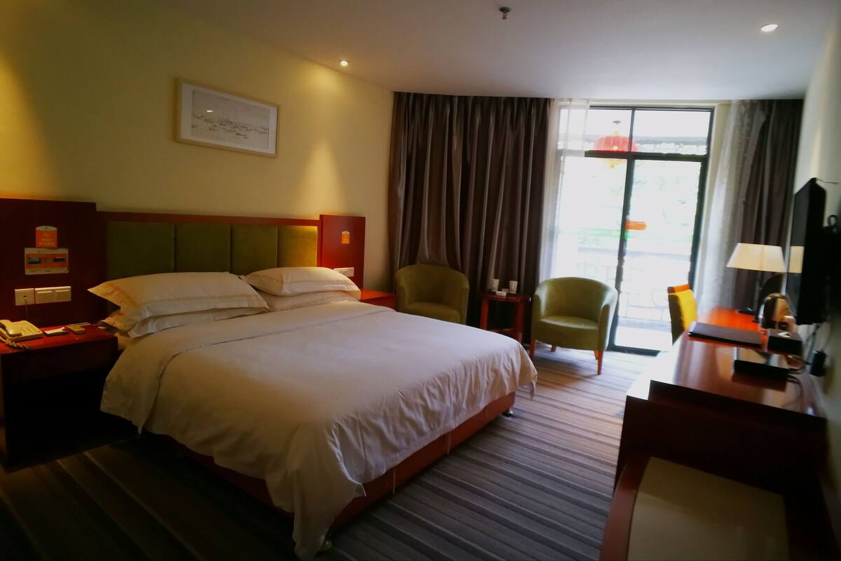 A hotel room with a large bed, two chairs, a desk, a TV, and a window with curtains.