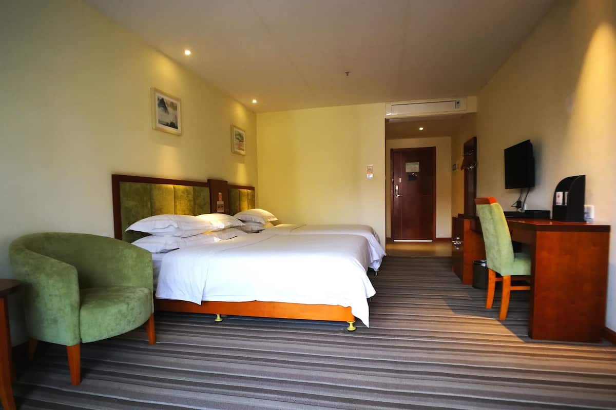 A hotel room with two beds, a desk, a chair, a television, and an air conditioning unit.