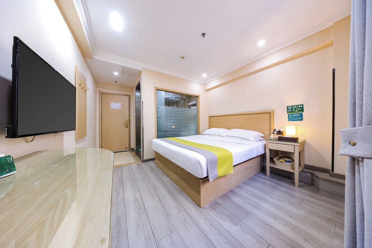 A hotel room with a bed, bedside table, TV, and a sign indicating WiFi availability.