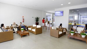 A modern lobby with wicker furniture, a flat-screen TV, and a glass entrance. - Everest Flat Service (Caldas Novas)