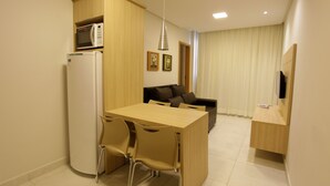 A compact living space with a kitchenette, a dining area with chairs, a sofa, and a television. - Everest Flat Service (Caldas Novas)